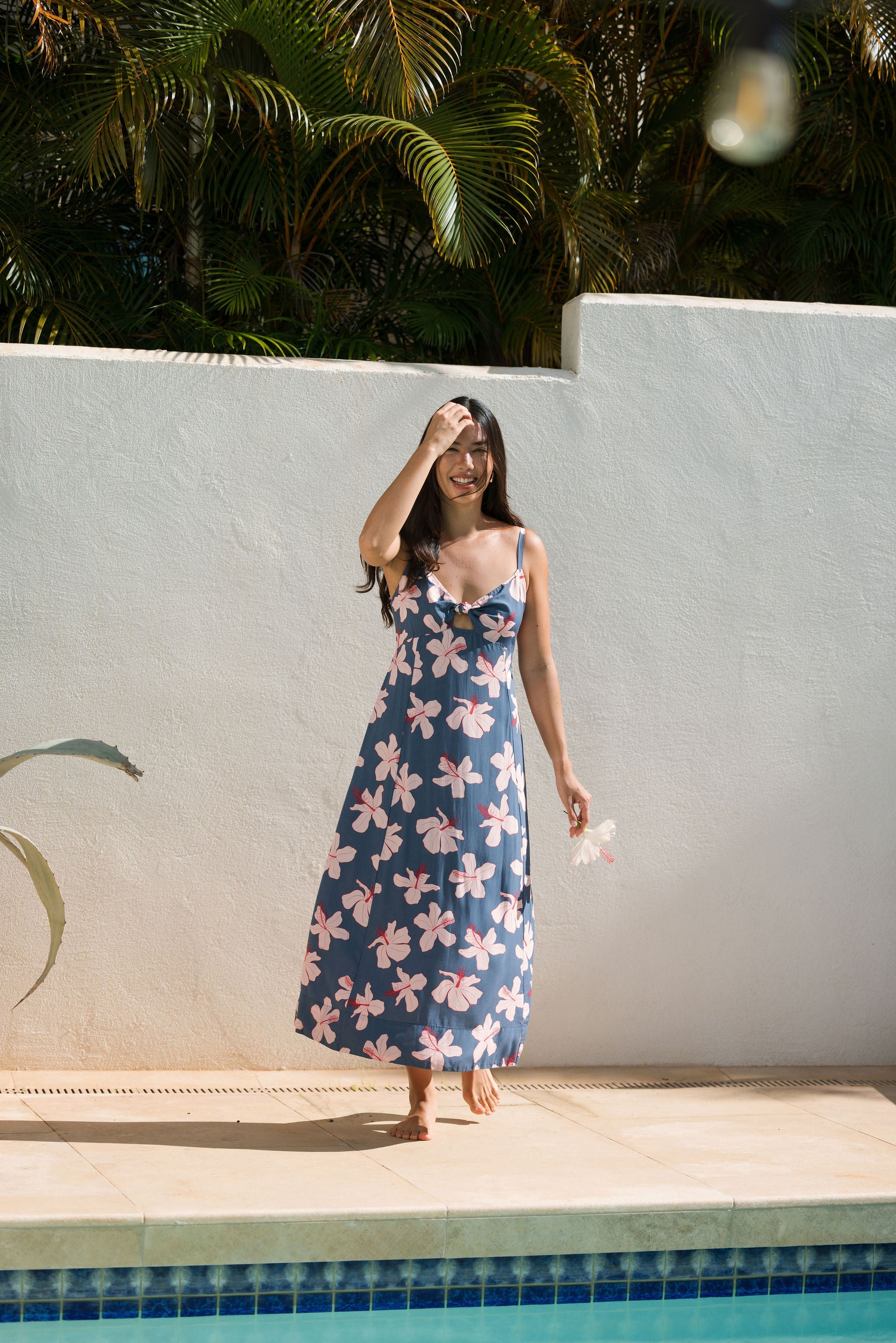 woman with black hair wearing a maxi dress with knot cutout neckline in a navy and pink hibiscus print.
