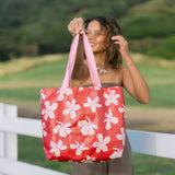 Woman with tote bag with beige and pink hibiscus print on orange red ground.