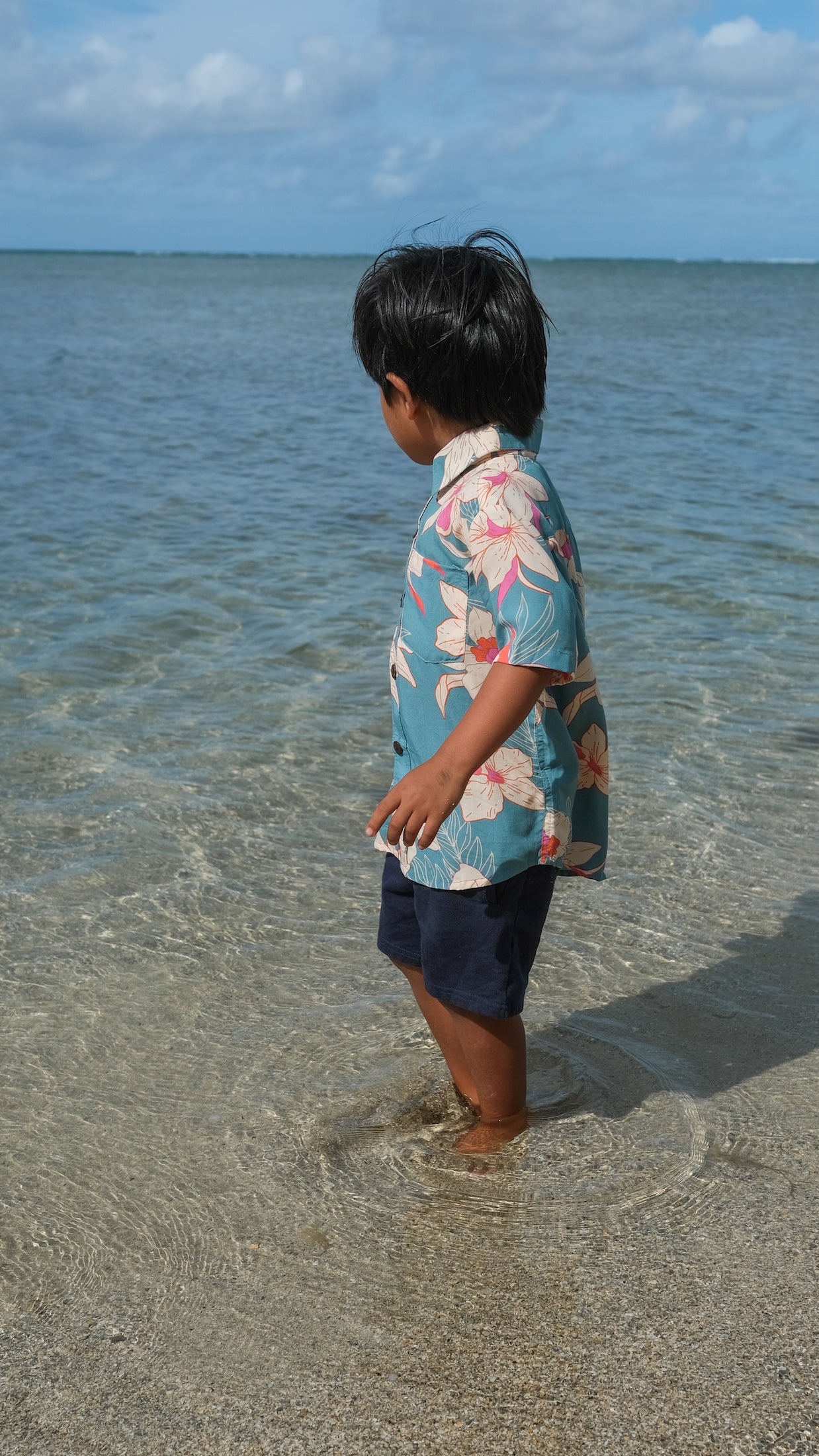 little boy wearing a teal aloha shirt with cream colored orchid blossom pattern