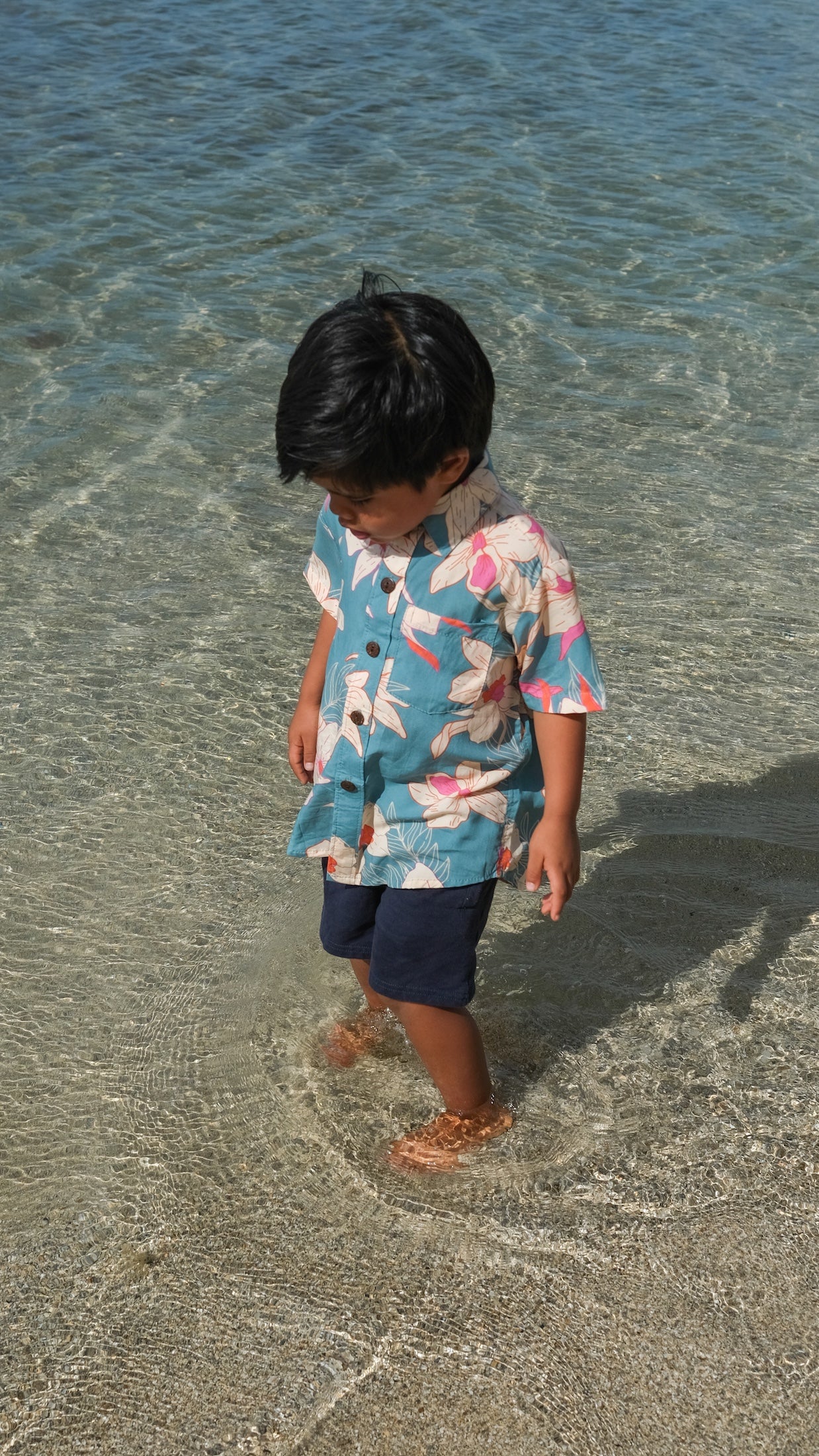 little boy wearing a teal aloha shirt with cream colored orchid blossom pattern
