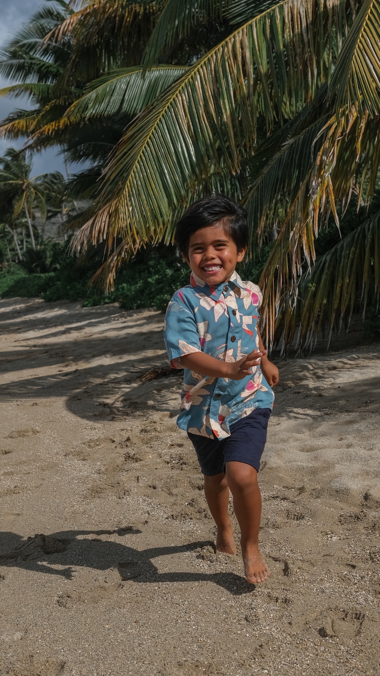 little boy wearing a teal aloha shirt with cream colored orchid blossom pattern