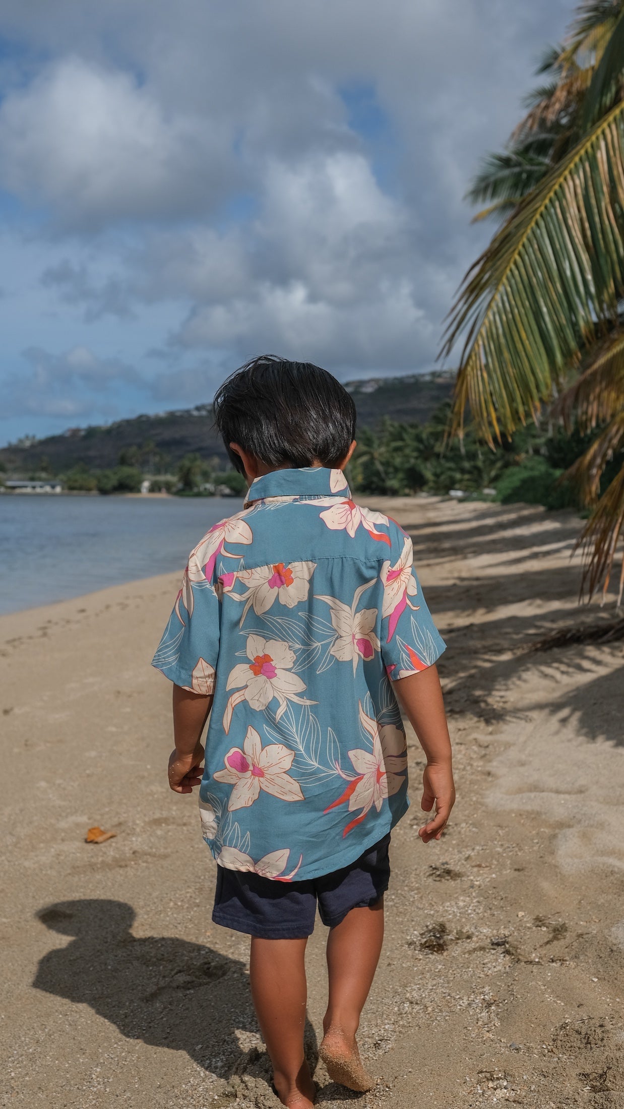little boy wearing a teal aloha shirt with cream colored orchid blossom pattern