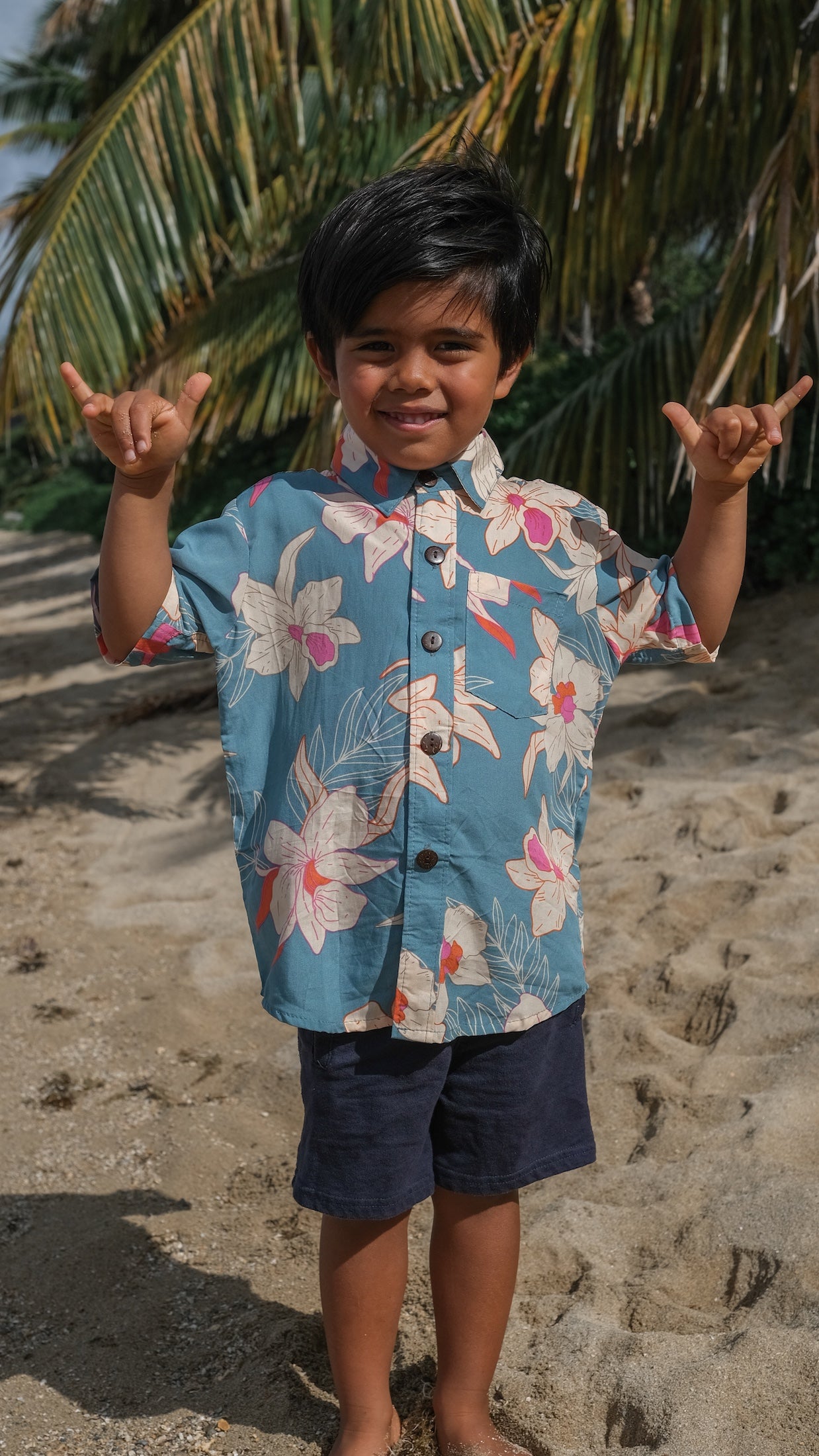 little boy wearing a teal aloha shirt with cream colored orchid blossom pattern