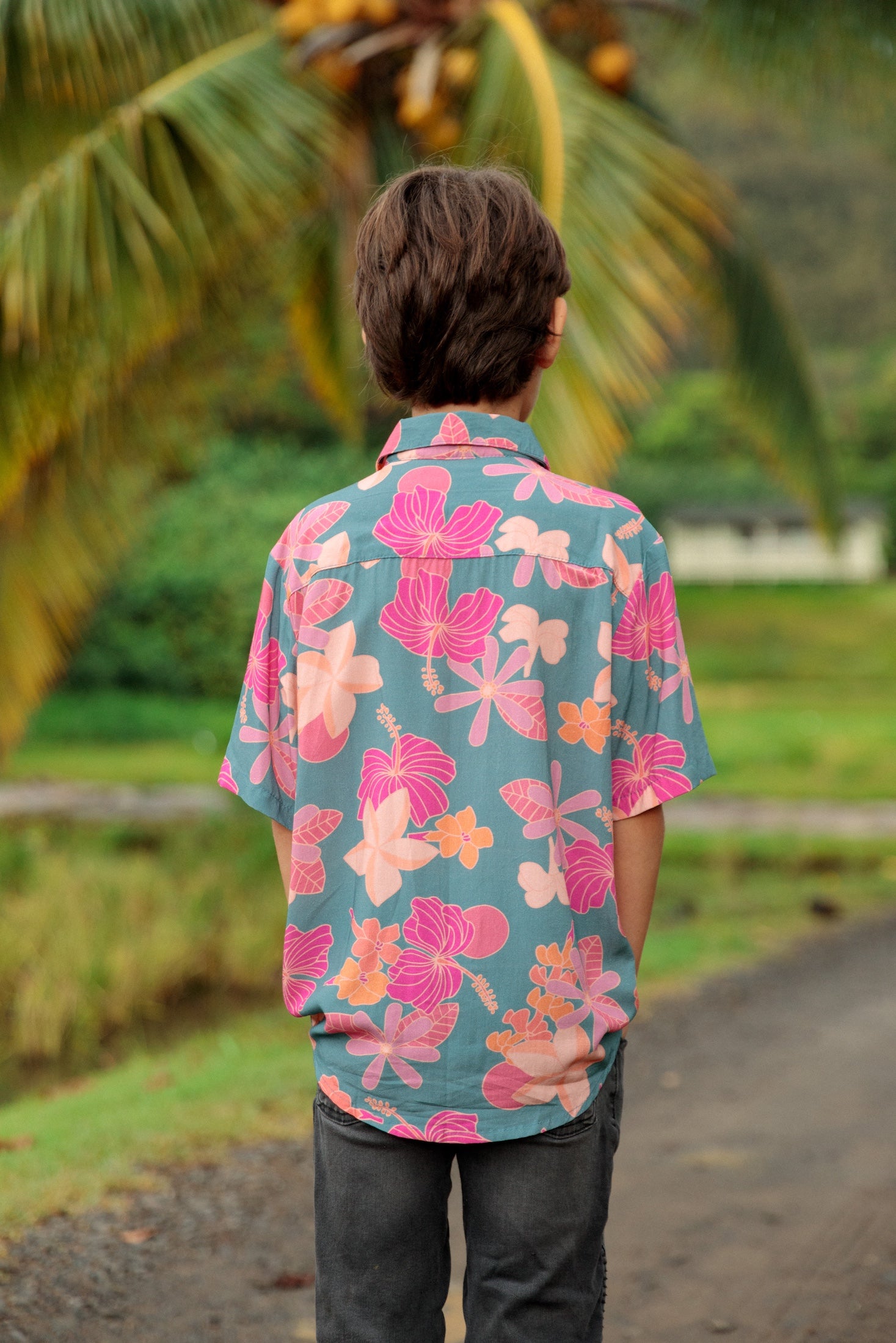 little boy wearing a teal button up aloha shirt with floral pattern