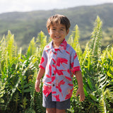 little boy with brown hair wearing a button up aloha shirt with periwinkle background and bright red hibiscus print.