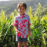 little boy with brown hair wearing a button up aloha shirt with periwinkle background and bright red hibiscus print.