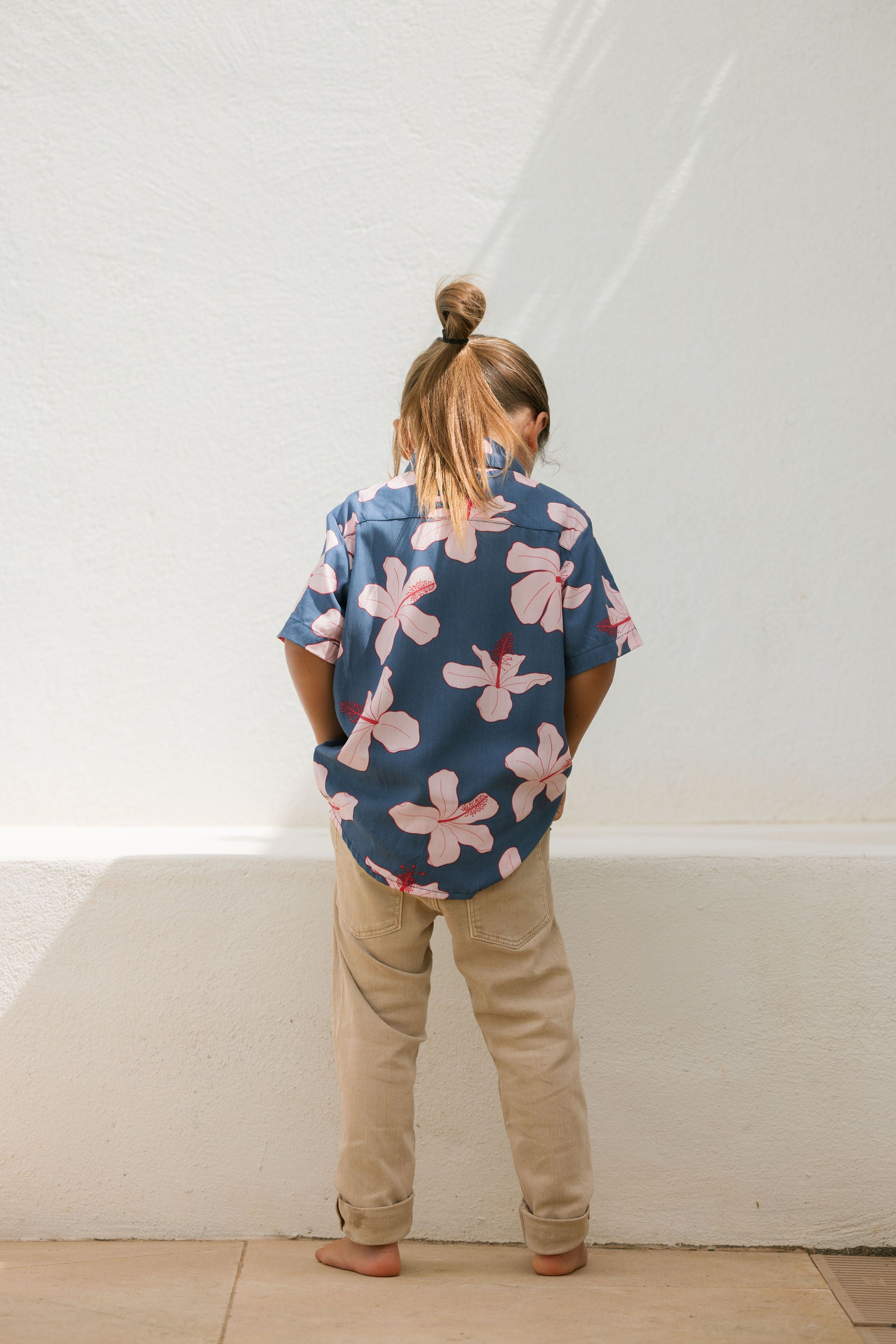 little boy wearing button up aloha shirt in navy and pink hibiscus print.