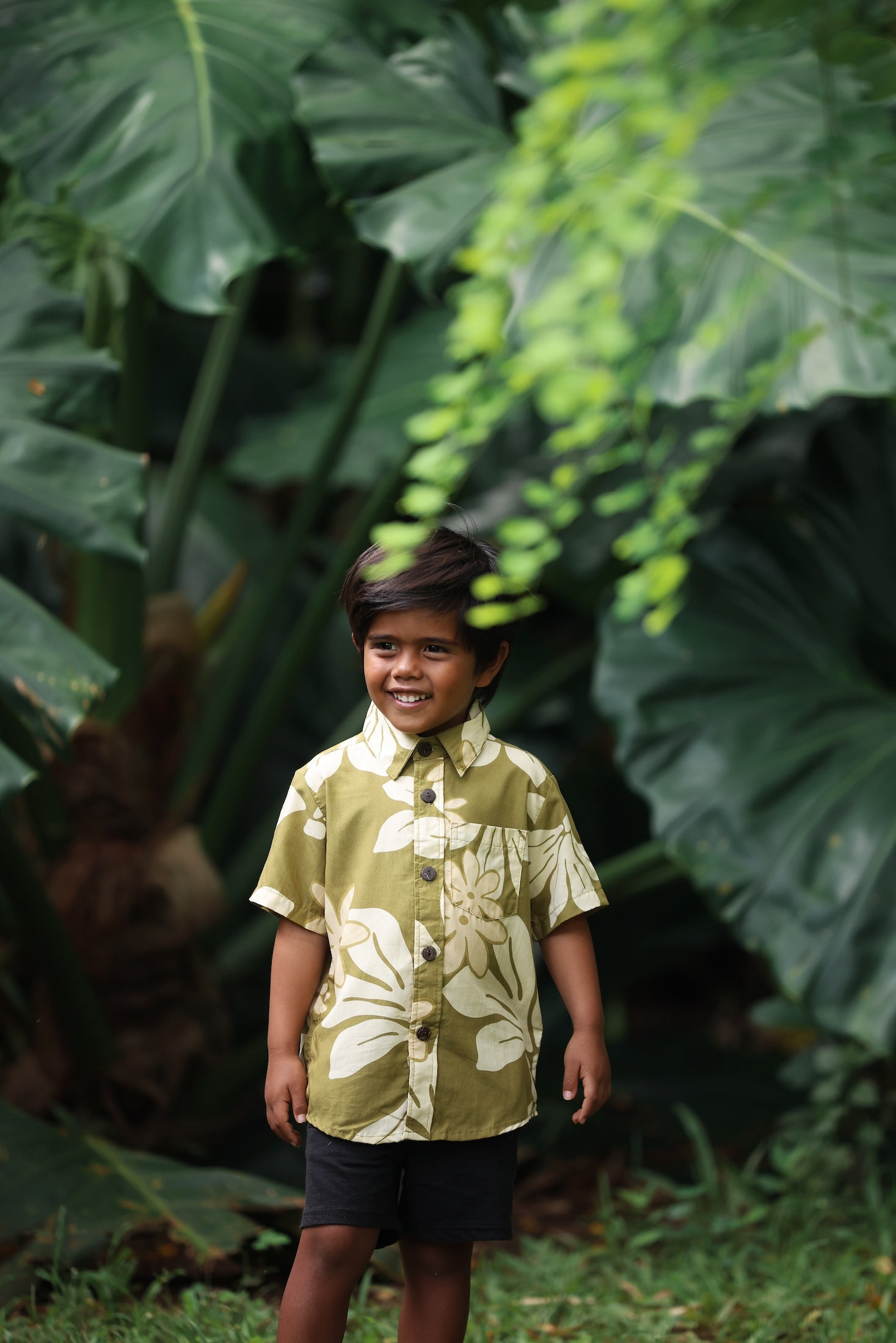 little boy wearing mini aloha button up shirt in green print and naupaka pattern