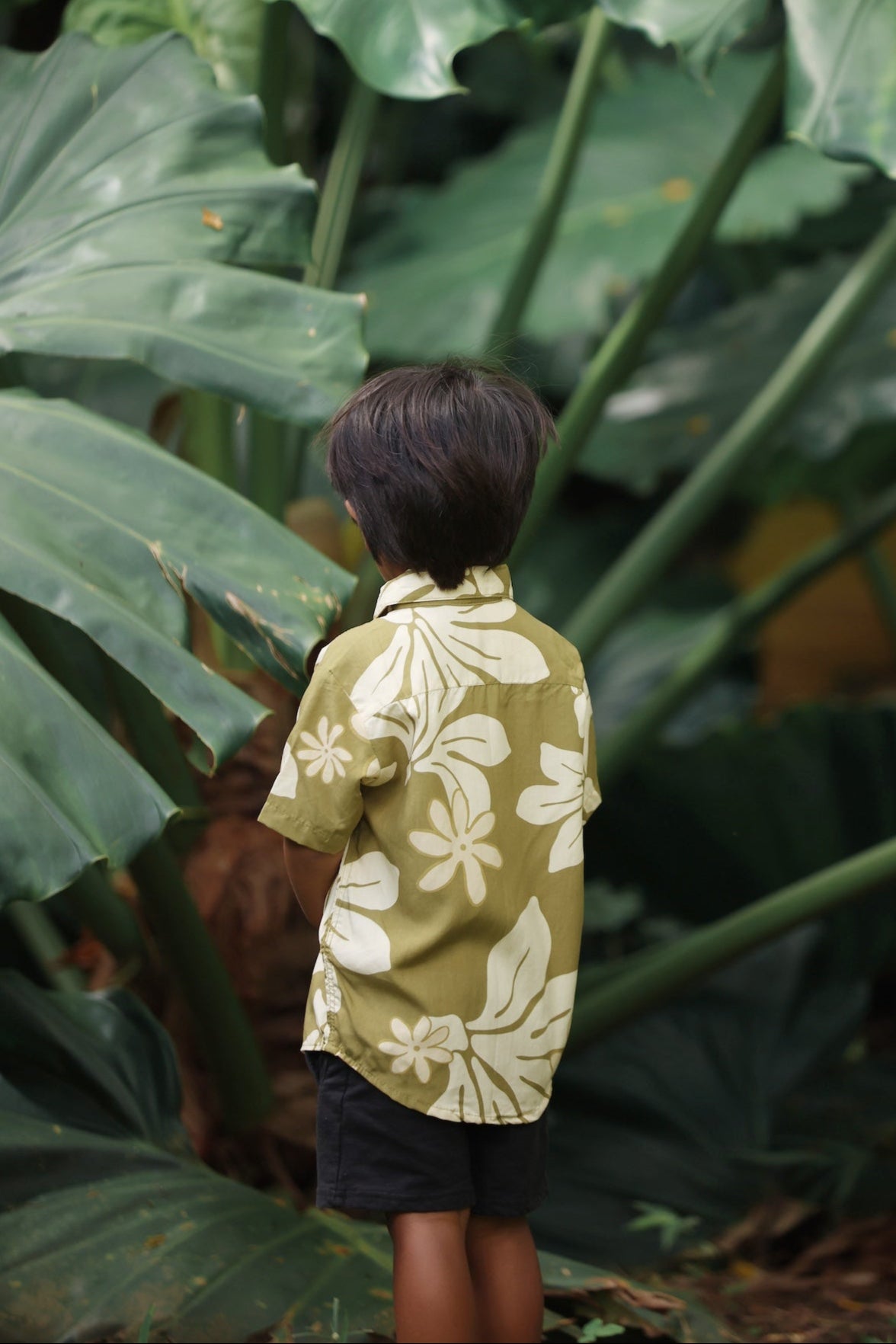 little boy wearing mini aloha button up shirt in green print and naupaka pattern