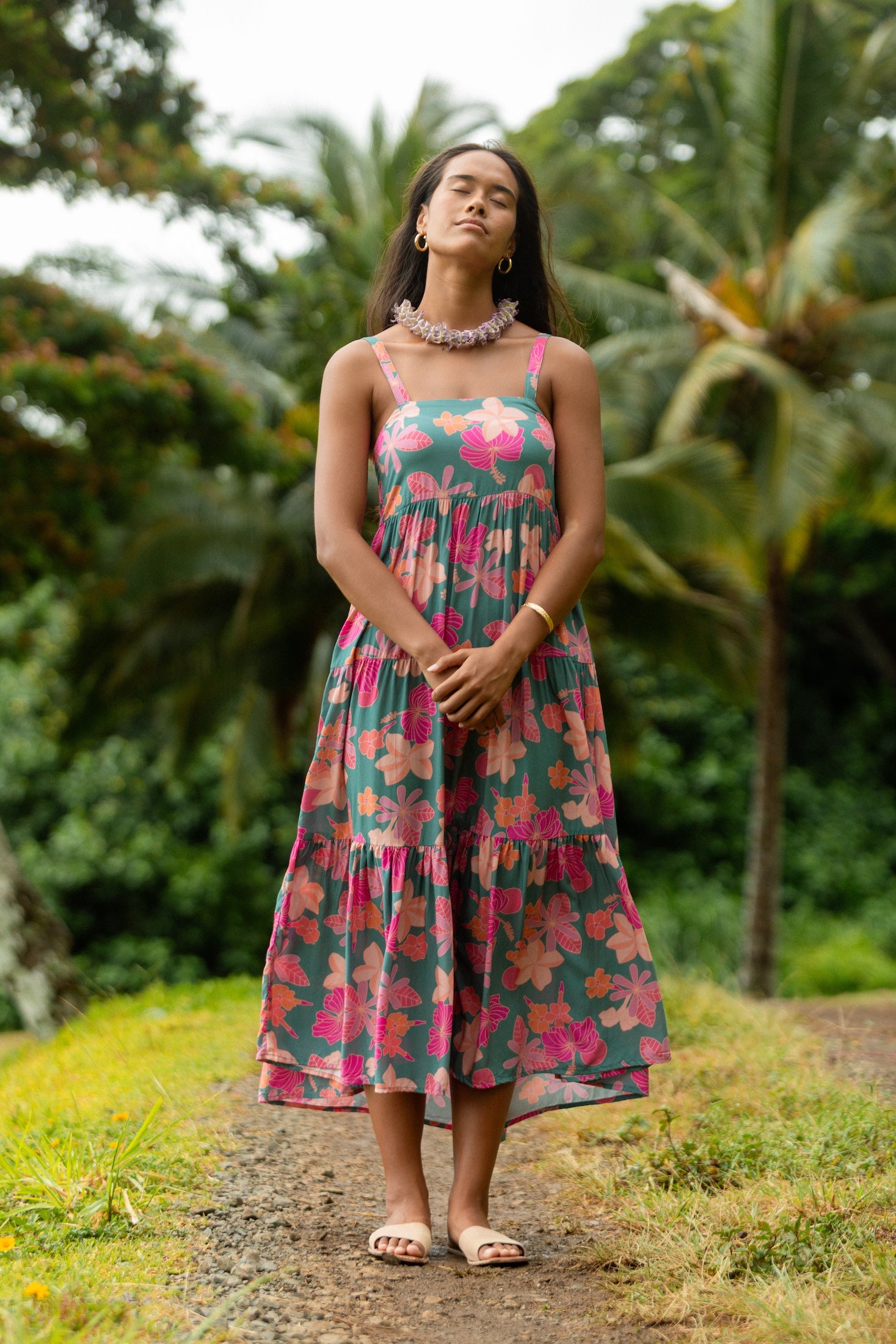 woman with brown hair wearing a teal maxi dress with orange and pink floral print