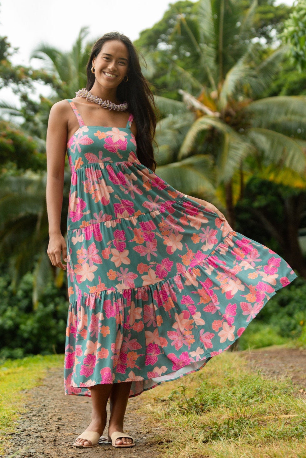 woman with brown hair wearing a teal maxi dress with orange and pink floral print