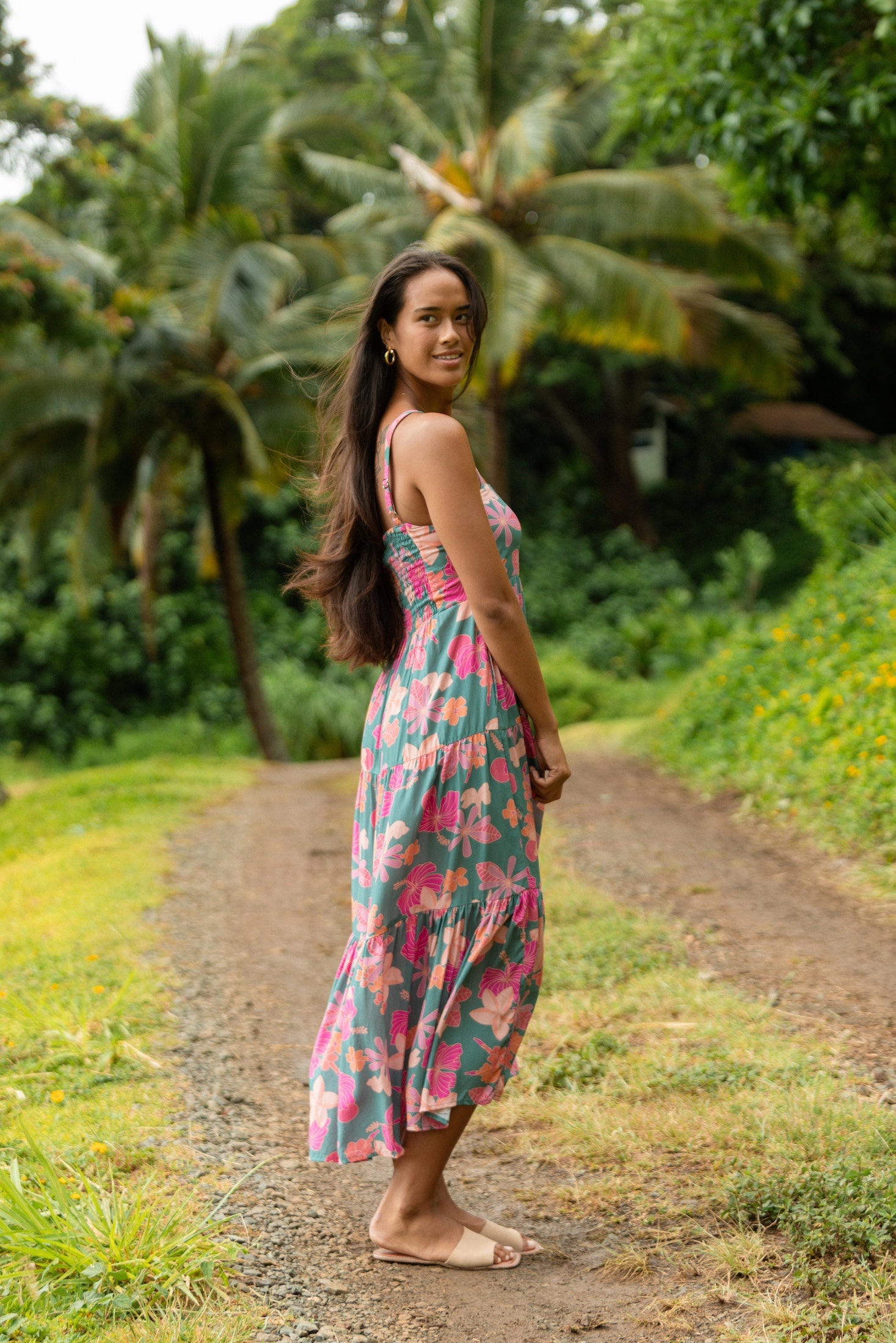 woman with brown hair wearing a teal maxi dress with orange and pink floral print