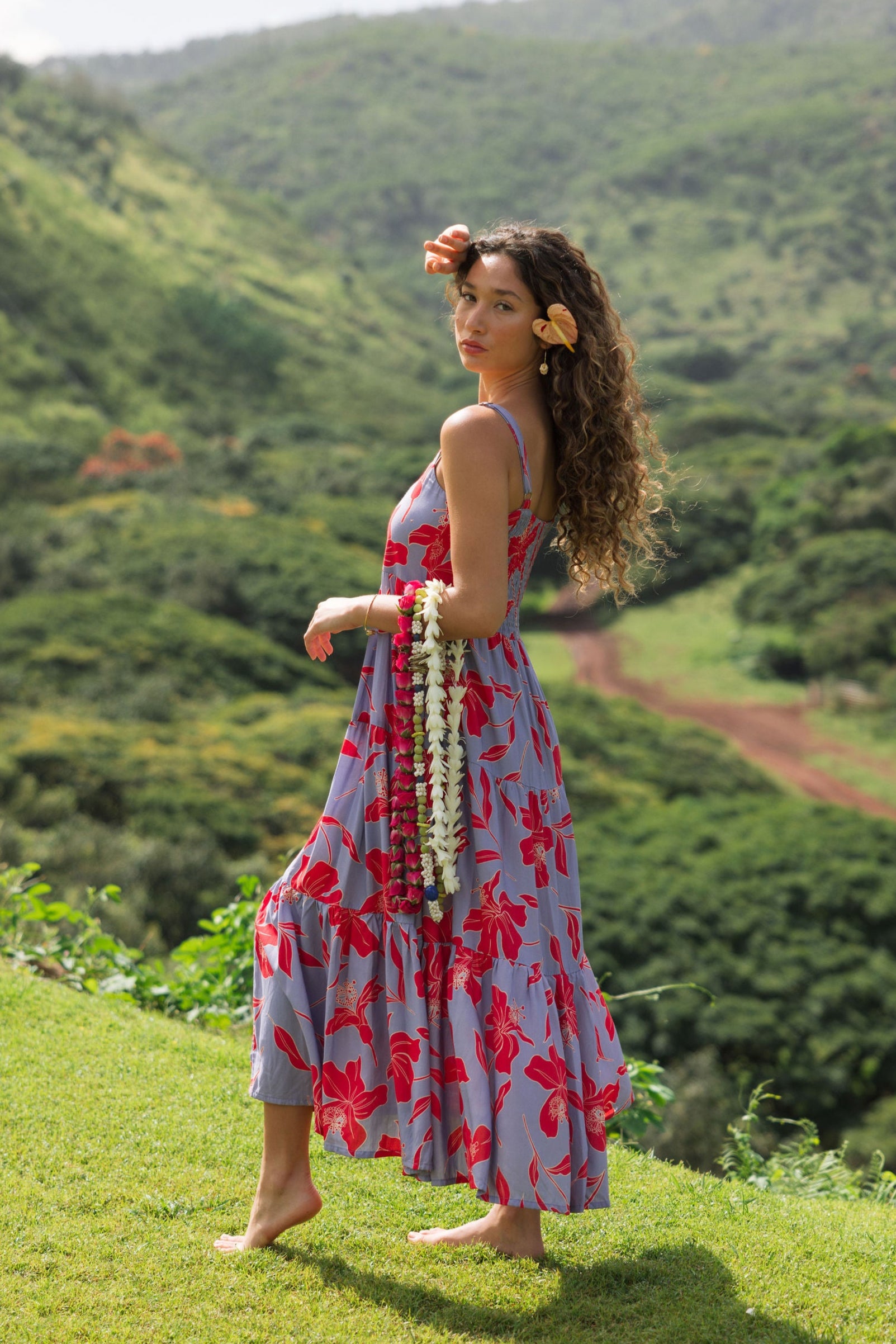 woman with brown hair wearing a flowy maxi dress with periwinkle background and bright red hibiscus print.