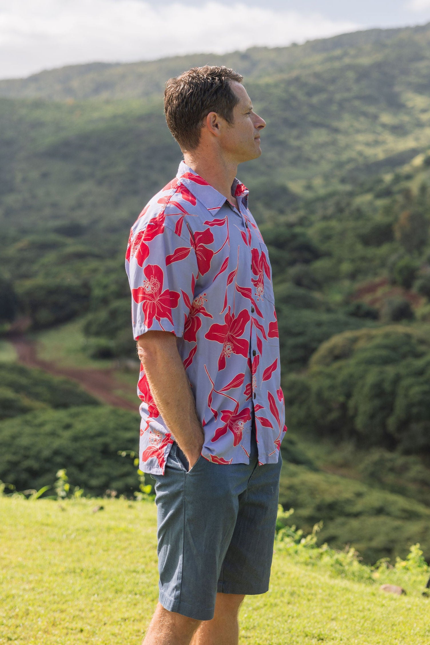 man with brown hair wearing a button up aloha shirt with periwinkle background and bright red hibiscus print.