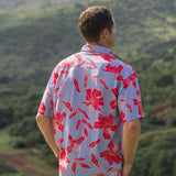 man with brown hair wearing a button up aloha shirt with periwinkle background and bright red hibiscus print.