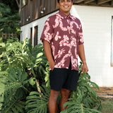 man wearing brown aloha shirt with pink lei awapuhi print