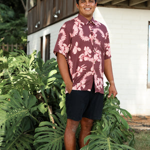 man wearing brown aloha shirt with pink lei awapuhi print