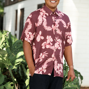 man wearing brown aloha shirt with pink lei awapuhi print
