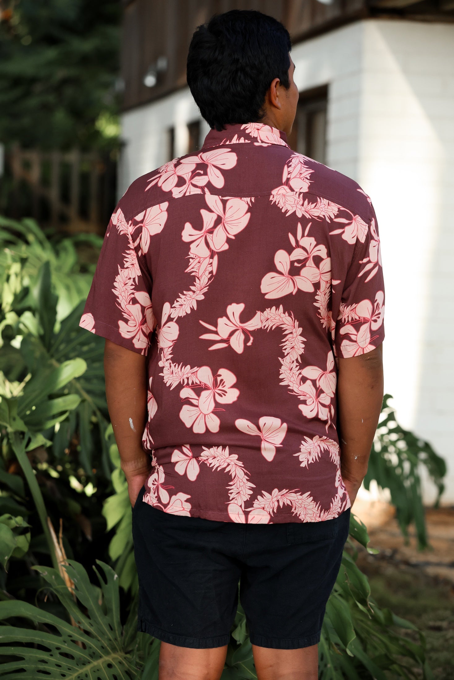 man wearing brown aloha shirt with pink lei awapuhi print