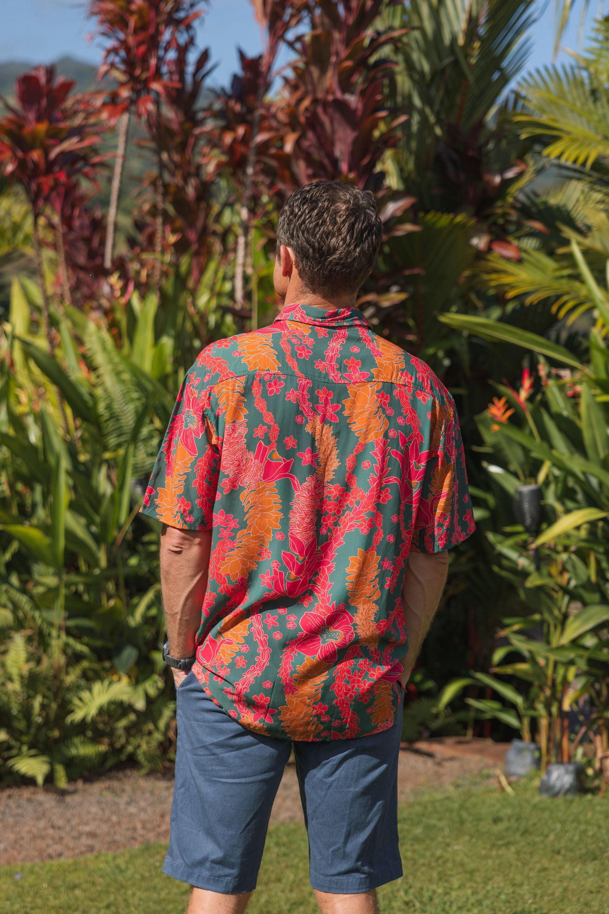 man with brown hair wearing a colorful button up aloha shirt with tropical lei print