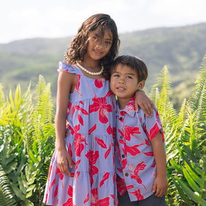 little girl with brown hair wearing a mid length dress with periwinkle background and bright red hibiscus print.