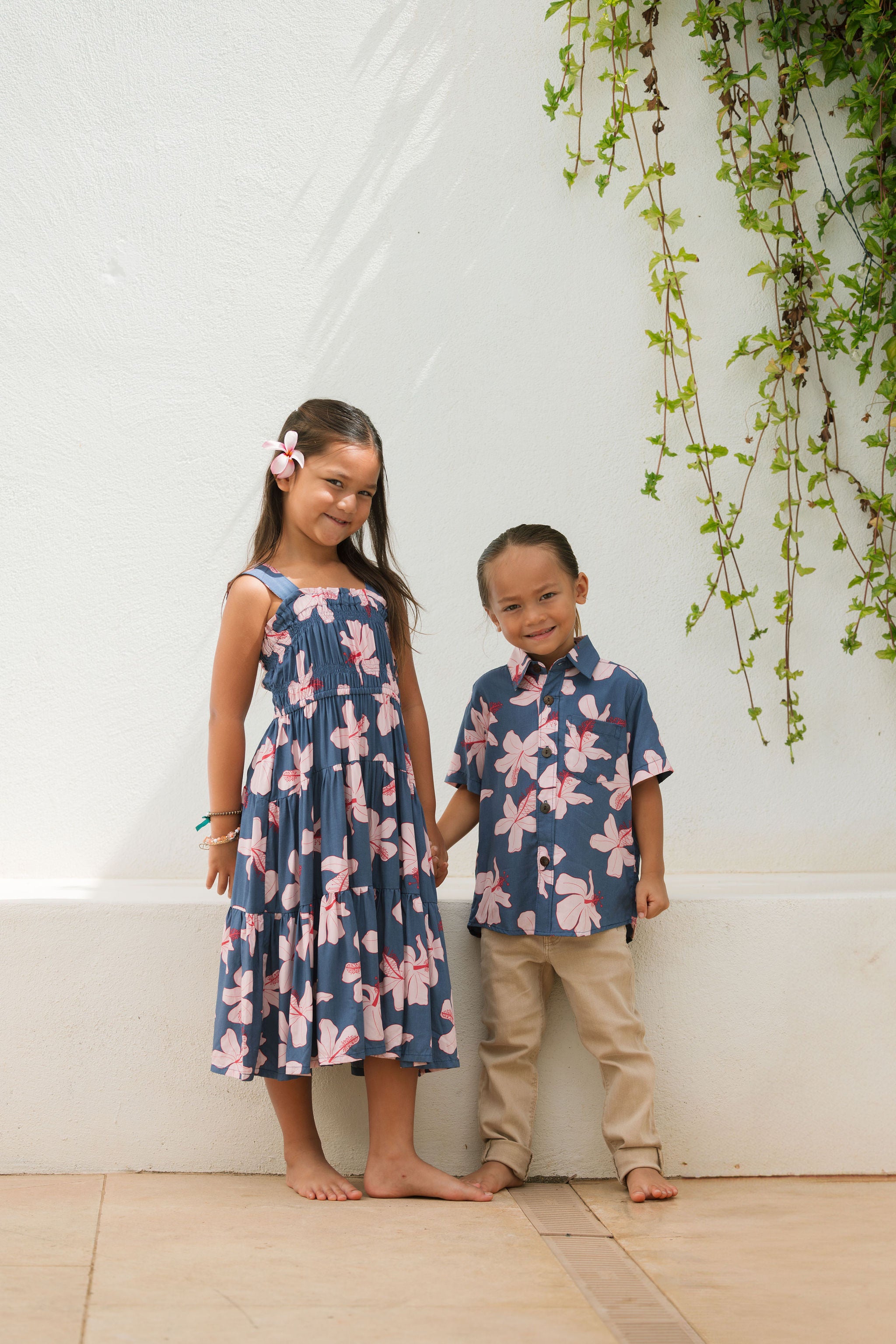 little boy wearing button up aloha shirt in navy and pink hibiscus print.