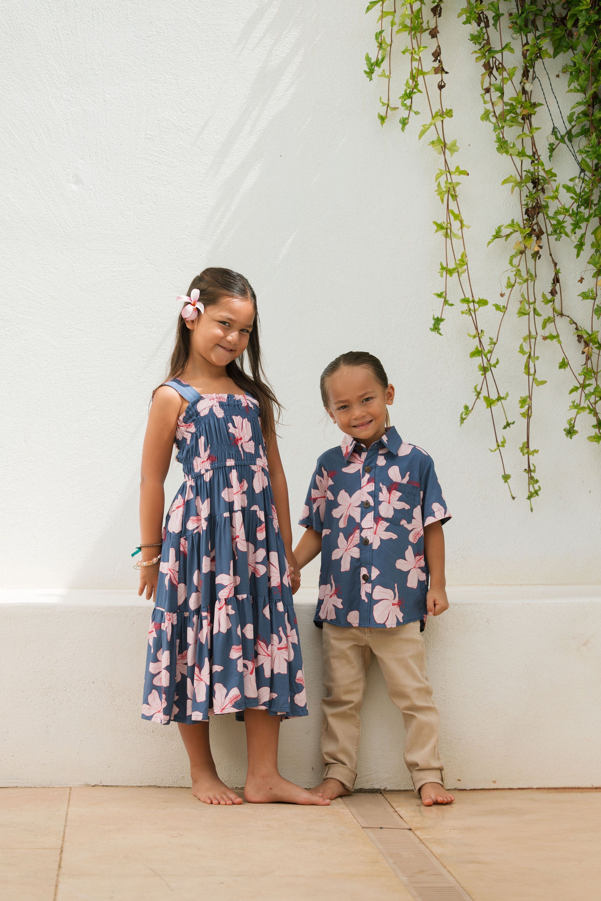 little boy wearing button up aloha shirt in navy and pink hibiscus print.