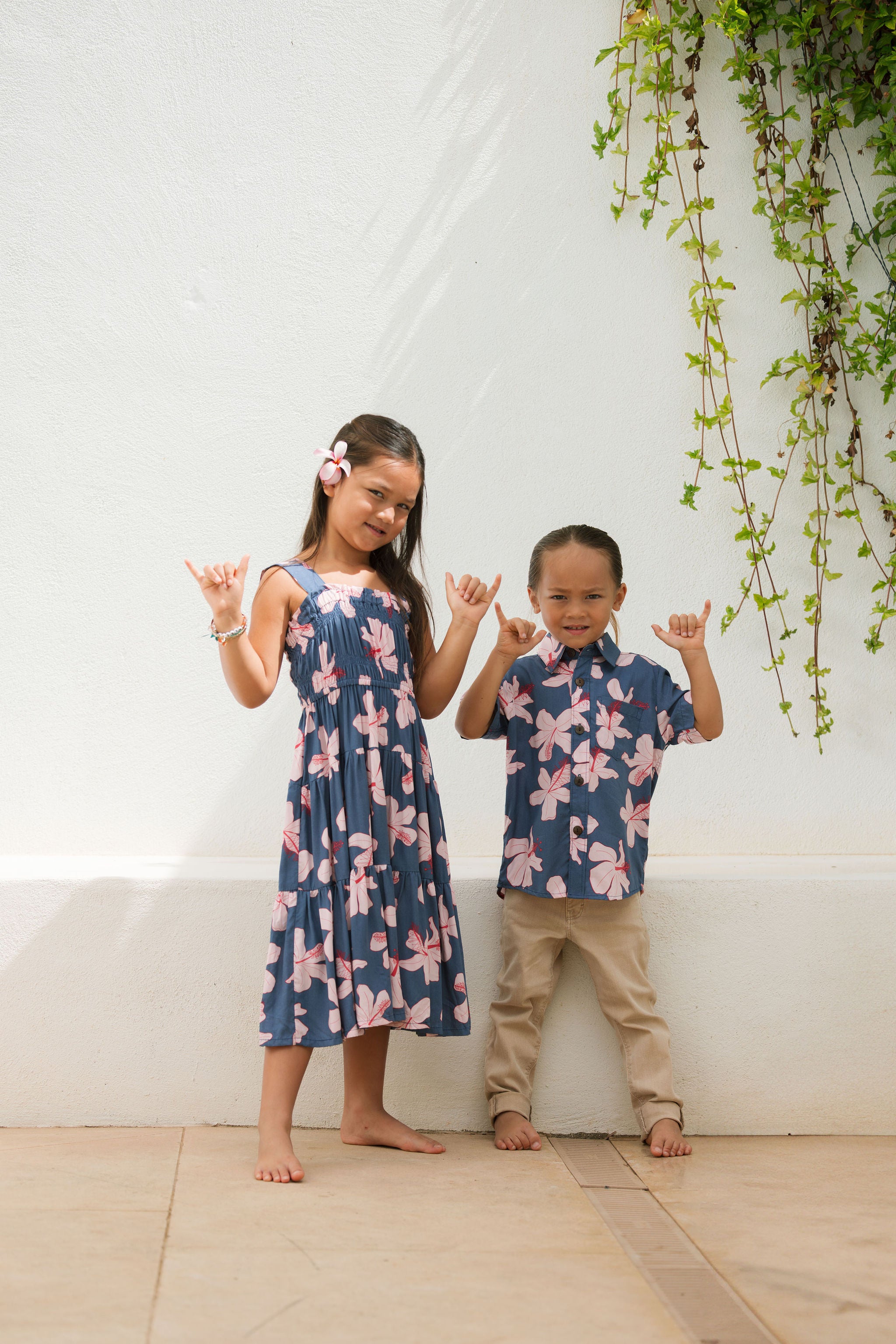 little boy wearing button up aloha shirt in navy and pink hibiscus print.