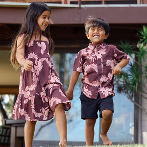 little girl wearing a long brown dress with tie sleeve with light pink lei awapuhi print and little boy wearing brown button-up with light pink lei awapuhi print