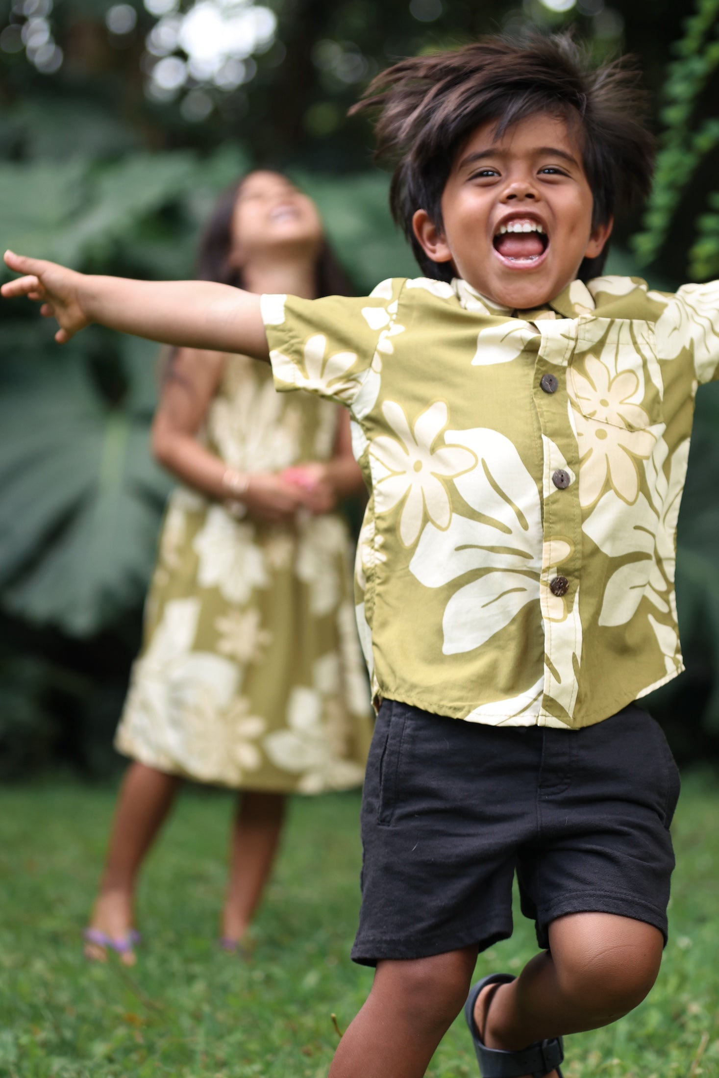 little boy wearing mini aloha button up shirt in green print and naupaka pattern