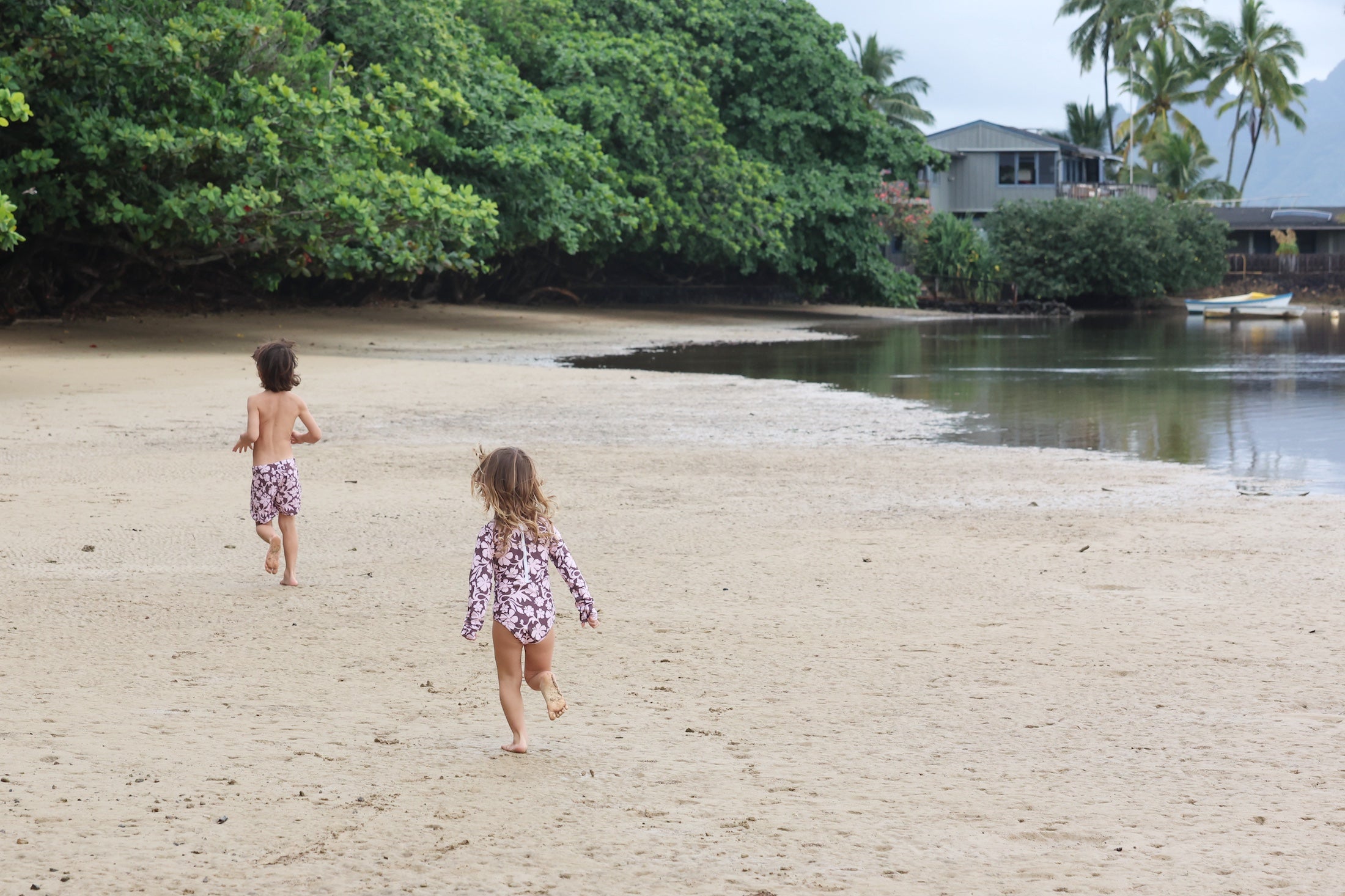 little boy wearing board shorts in blush and brown hibiscus print.