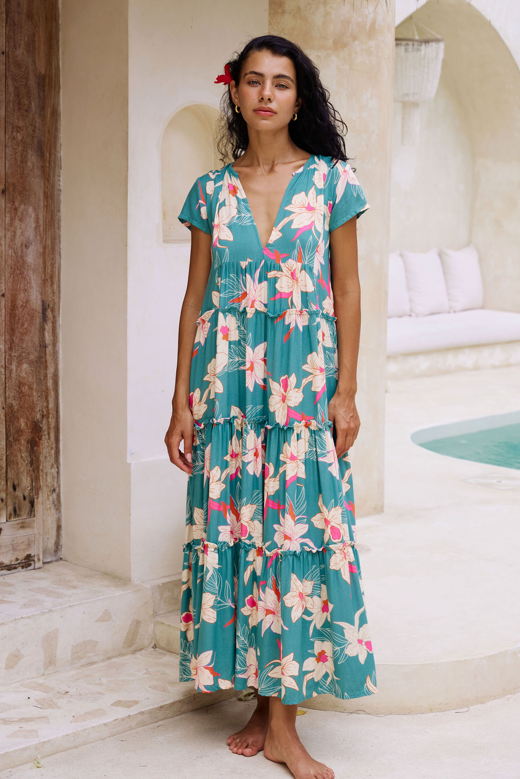 woman with brown hair wearing a tiered maxi dress in teal with large cream colored orchids.