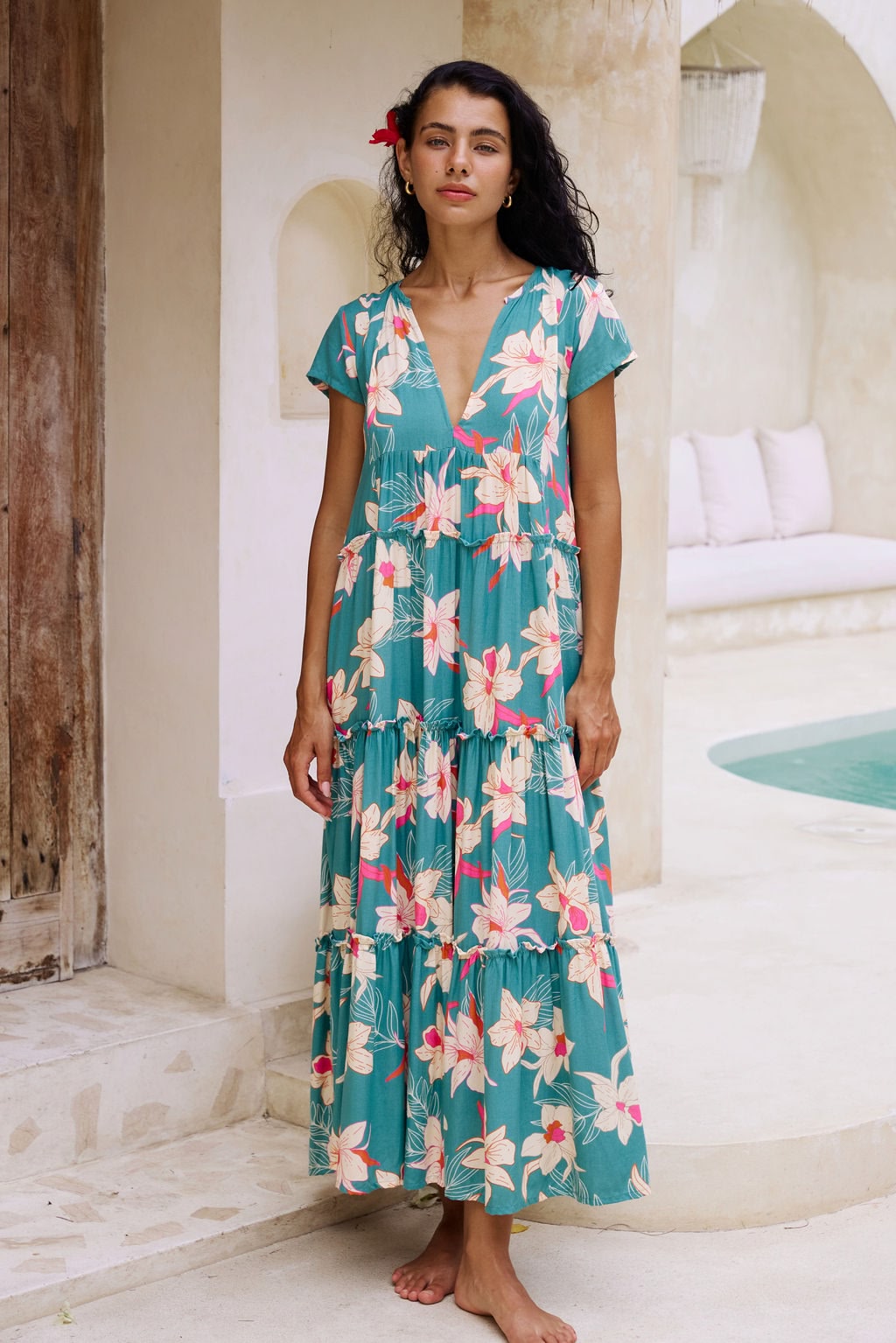 woman with brown hair wearing a tiered maxi dress in teal with large cream colored orchids.