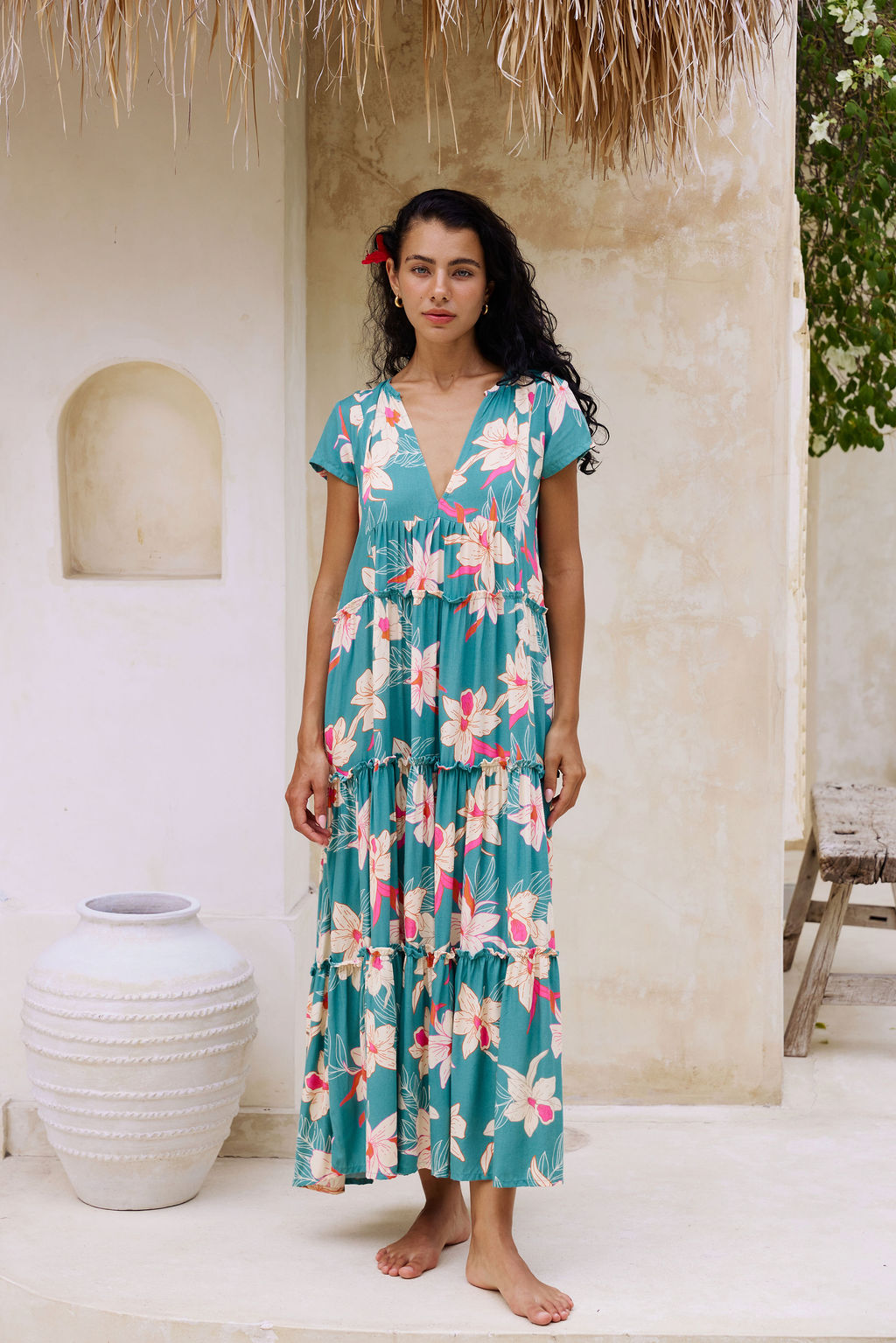 woman with brown hair wearing a tiered maxi dress in teal with large cream colored orchids.