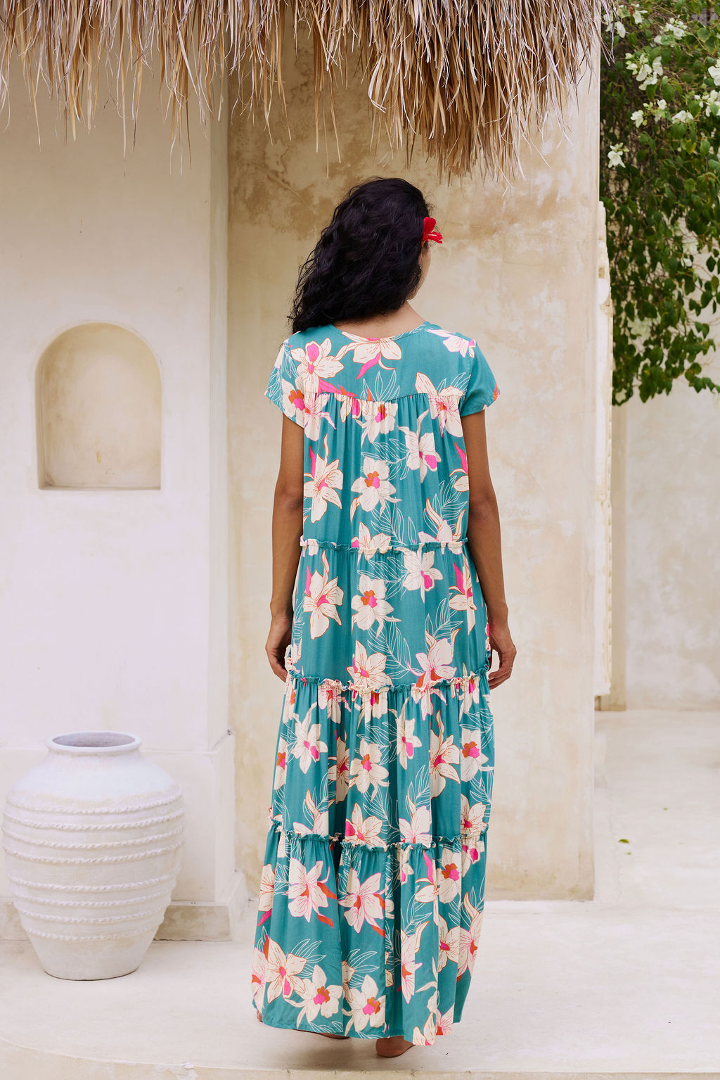 woman with brown hair wearing a tiered maxi dress in teal with large cream colored orchids.