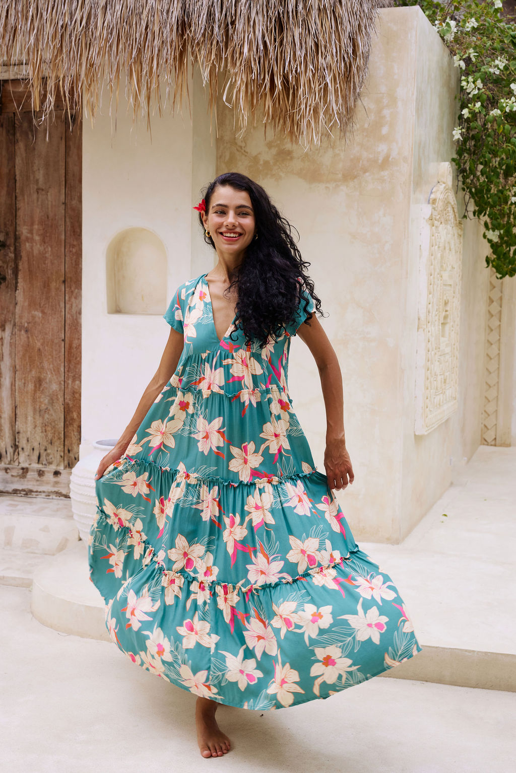 woman with brown hair wearing a tiered maxi dress in teal with large cream colored orchids.
