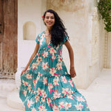 woman with brown hair wearing a tiered maxi dress in teal with large cream colored orchids.