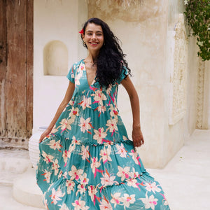 woman with brown hair wearing a tiered maxi dress in teal with large cream colored orchids.
