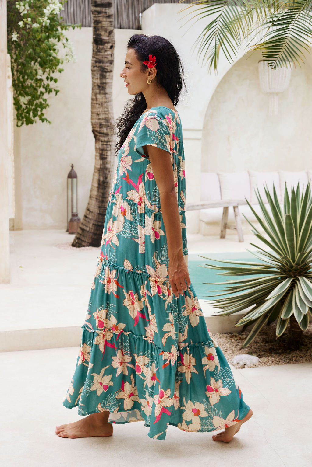 woman with brown hair wearing a tiered maxi dress in teal with large cream colored orchids.