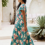 woman with brown hair wearing a tiered maxi dress in teal with large cream colored orchids.