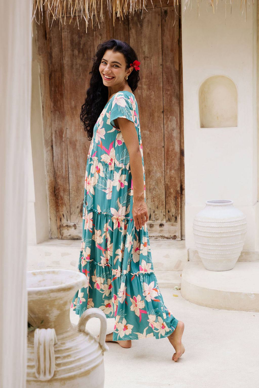 woman with brown hair wearing a tiered maxi dress in teal with large cream colored orchids.
