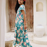 woman with brown hair wearing a tiered maxi dress in teal with large cream colored orchids.