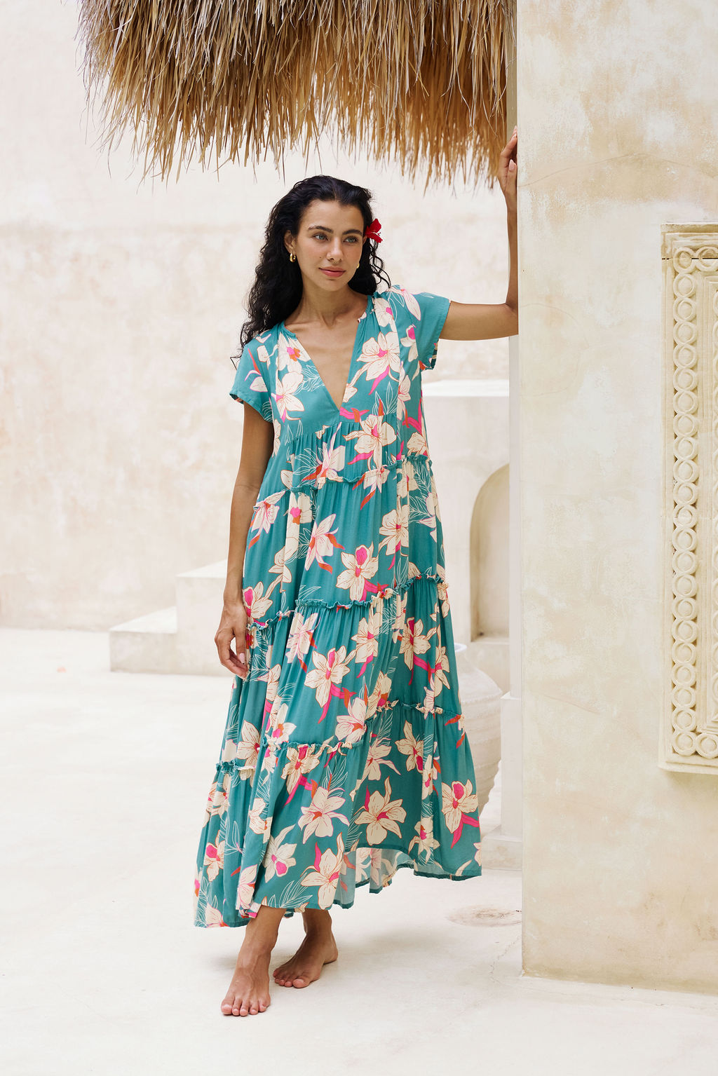 woman with brown hair wearing a tiered maxi dress in teal with large cream colored orchids.