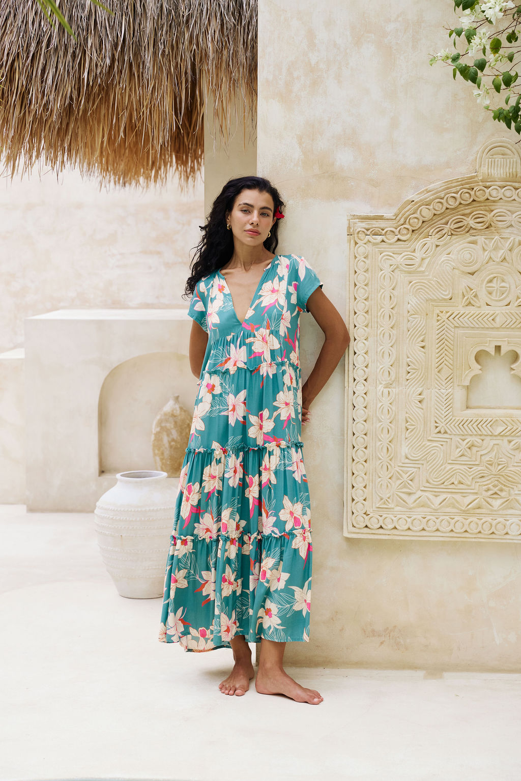 woman with brown hair wearing a tiered maxi dress in teal with large cream colored orchids.