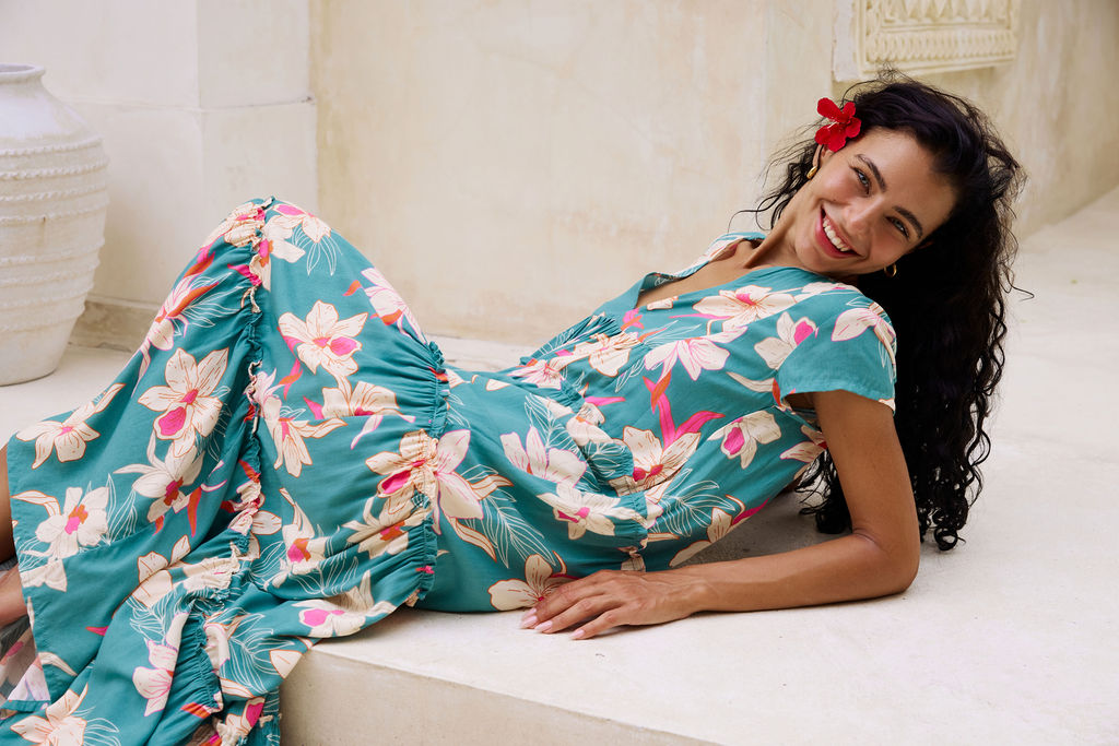 woman with brown hair wearing a tiered maxi dress in teal with large cream colored orchids.