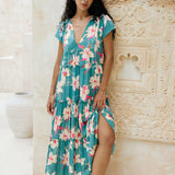 woman with brown hair wearing a tiered maxi dress in teal with large cream colored orchids.