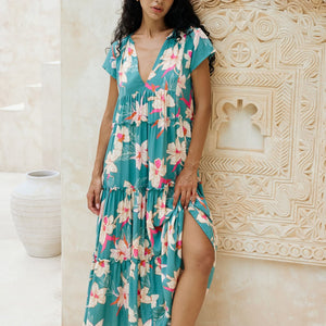 woman with brown hair wearing a tiered maxi dress in teal with large cream colored orchids.