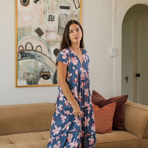 woman with black hair wearing a tiered maxi dress with v neckline in a navy and pink hibiscus print.