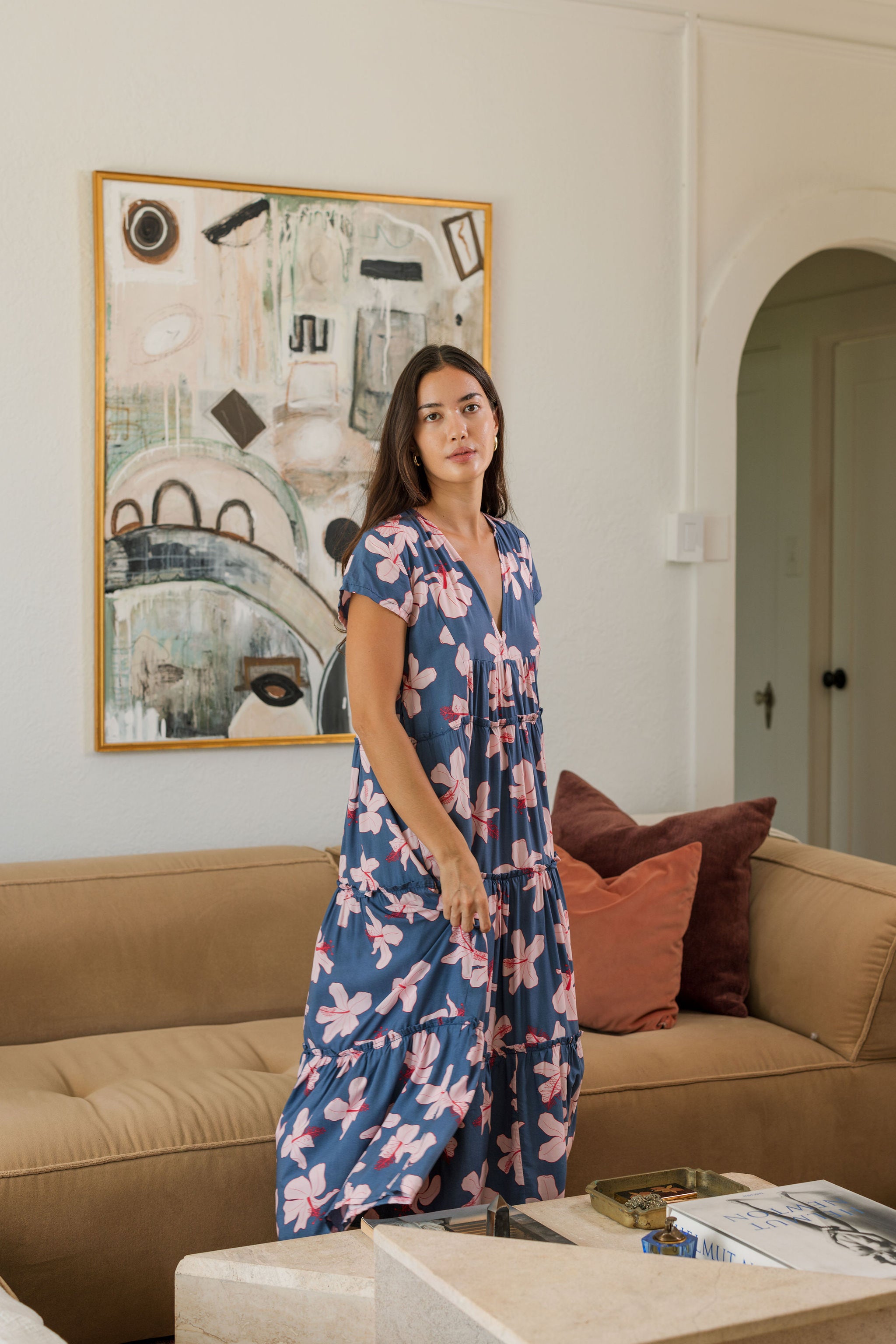 woman with black hair wearing a tiered maxi dress with v neckline in a navy and pink hibiscus print.