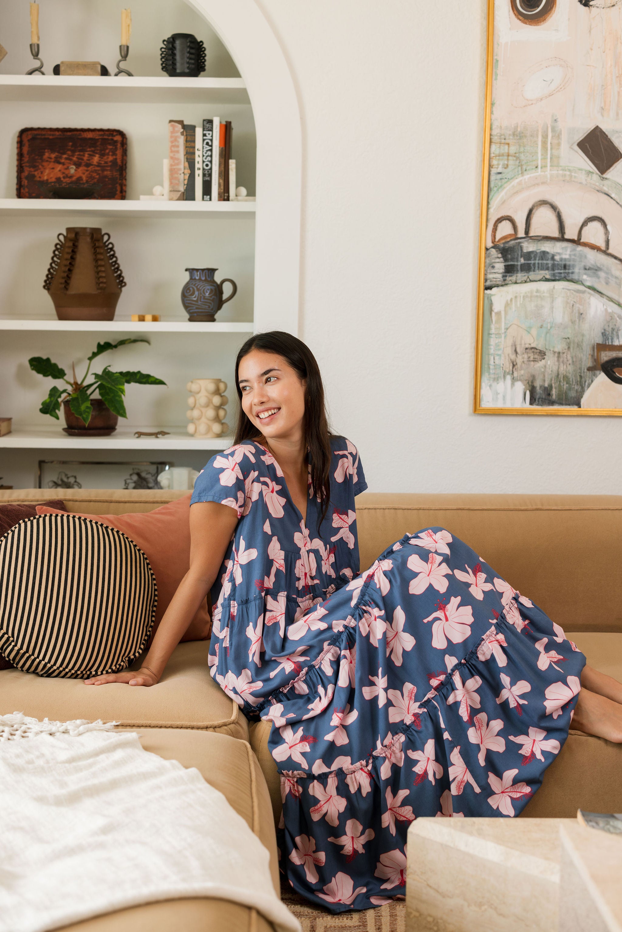 woman with black hair wearing a tiered maxi dress with v neckline in a navy and pink hibiscus print.